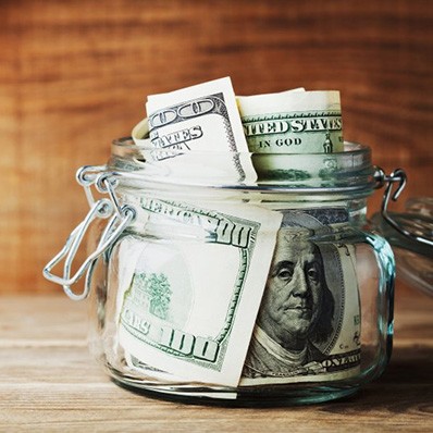 Money inside a glass jar that’s sitting on a wood surface